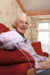 Side shot of an old bespectacled lady sitting on the couch knitting