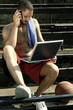 A man sitting on the stairs talking on the hand phone while using his laptop