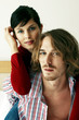 A guy carrying his girlfriend on his back while sitting on the bed