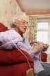 Side shot of an old bespectacled lady sitting on the couch knitting