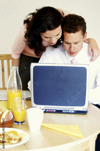 Photo: A woman watching her husband playing with his laptop on the dining table A woman watching her husband playing with his laptop on the dining table