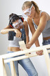 A woman helping her friend to hold the wood as she is drilling