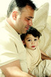 A man sitting on the couch together with his son who is looking at the camera