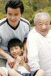 A boy sitting in the park with his father and grandfather