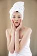 A woman with her hair and body wrapped up in towel touching her face with her hands