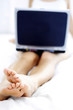 Shoulder down shot of a woman sitting on the bed with a laptop on her lap