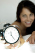 Woman lying on the bed showing an alarm clock 