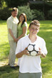 Teenage boy holding a soccer ball with his parents standing in the background