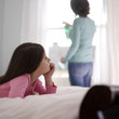 Girl daydreaming on the bed while her mother is cleaning the window