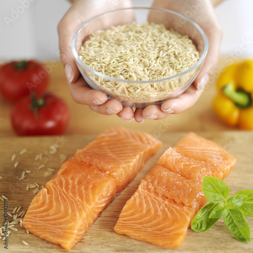 Photo: Woman's hands holding a bowl of brown rice, raw salmon with bell pepper and tomatoes on wooden chopping board Woman's hands holding a bowl of brown rice, raw salmon with bell pepper and tomatoes on wooden chopping board