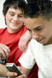 Boy text messaging on the phone, another boy watching