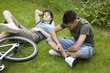 Boy text messaging on the phone, another boy resting on the grass