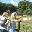 Man giving boy a piggy back ride while woman is pointing at ducks in a farm