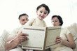 A man and a woman sitting on the couch reading a book for their son