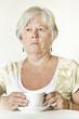 Thoughtful Senior lady sitting at table holding a cup of tea