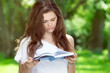 Beautiful young girl reads a book in the park