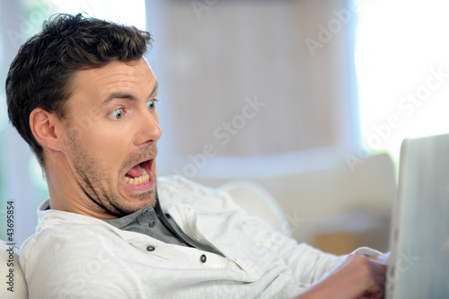 Foto: Man in sofa with scared look in front of tablet Man in sofa with scared look in front of tablet