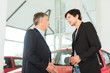 Mature dealer and young man with auto in car dealership