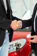 Handshake of two men in suits with a red car