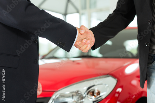 Photo: Handshake of two men in suits with a red car Handshake of two men in suits with a red car