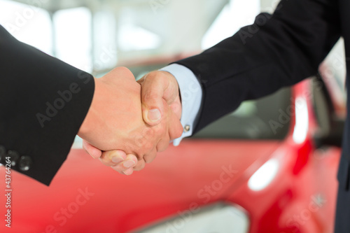 Photo: Handshake of two men in suits with a red car Handshake of two men in suits with a red car