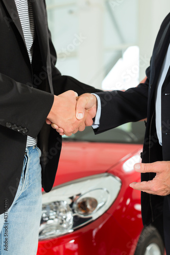 Photo: Handshake of two men in suits with a red car Handshake of two men in suits with a red car