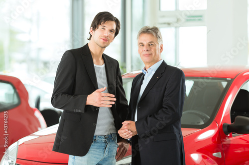 Photo: Mature and young man with autos in car dealership Mature and young man with autos in car dealership