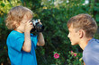 Little cute blond boy with a camera shoots her brother outdoors