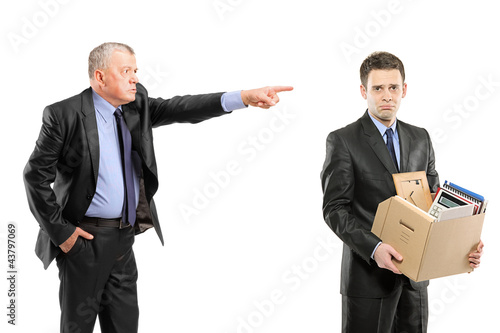 Foto: Angry boss firing a man carrying a box of personal items Angry boss firing a man carrying a box of personal items