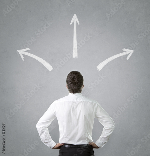 Photo: Confused, young businessman looking at chalk drawn arrows Confused, young businessman looking at chalk drawn arrows