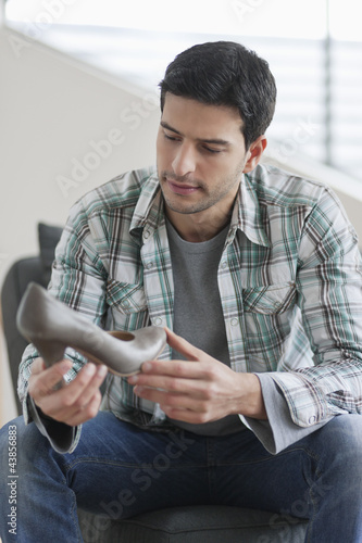 Photo: Man sitting on a couch and holding a high heel shoe Man sitting on a couch and holding a high heel shoe