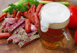 mug of beer and an assortment of salami and vegetables on a cutt