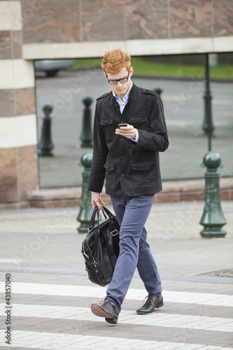 Photo: Businessman crossing a road while using a mobile phone Businessman crossing a road while using a mobile phone