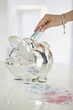 Person's hand putting money into a piggy bank