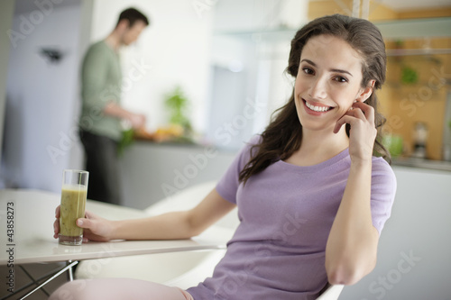 Photo: Woman drinking soup with her husband preparing food in the background Woman drinking soup with her husband preparing food in the background