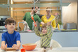 Children cooking in the kitchen with their parents in the background