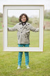 Portrait of a boy standing with a frame in a park