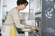 Elderly woman putting a tray of seafood into an oven
