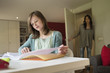 Girl studying with her mother standing at door in the background