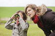 Boy looking through binoculars standing with his mother