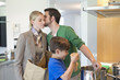 Man kissing his wife returning from shopping and son cooking in the kitchen