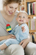 Baby girl sitting on the lap of her mother playing with a toy