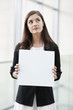 Businesswoman holding a blank placard and thinking in an office