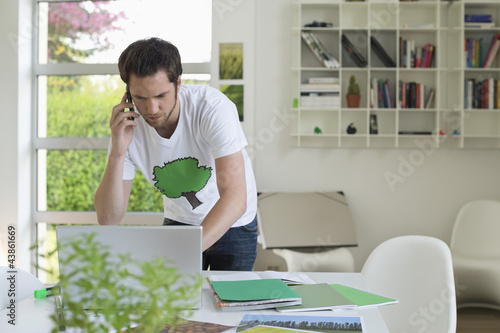 Photo: Man holding a mobile phone and working on a laptop Man holding a mobile phone and working on a laptop