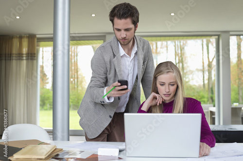 Photo: Woman working on a laptop with a man using mobile phone beside her Woman working on a laptop with a man using mobile phone beside her