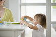 Foto: Cute little girl picking up toy tea set from a dining table Cute little girl picking up toy tea set from a dining table