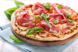 Pizza with cured ham topped with basil and rosemary