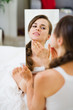 Happy young woman sitting on bed and looking on mirror