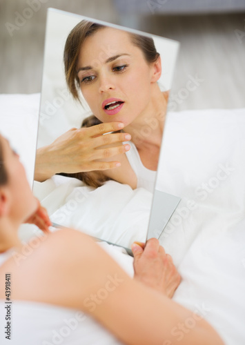 Photo: Young woman laying on bed and checking face in mirror Young woman laying on bed and checking face in mirror