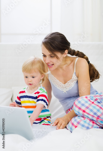 Photo: Modern young mother and baby using laptop Modern young mother and baby using laptop